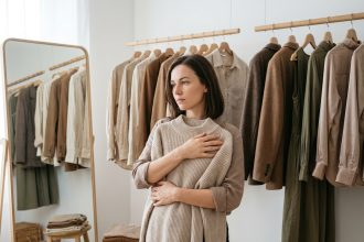 Femme tenant un pull dans son dressing, réfléchissant à l'organisation et à la sélection de ses vêtements avant de refaire sa garde-robe