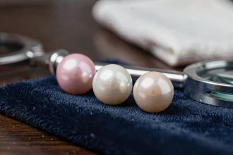 Gros plan sur trois perles de culture posées sur un velours bleu marine dans un atelier de joaillerie, illustrant la qualité et l'iridescence naturelle des vraies perles