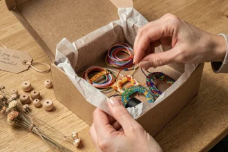 Femme arrangeant un kit de bracelets colorés dans une boîte cadeau kraft premium avec étiquette manuscrite et fleurs séchées